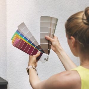 Uma fotografia tirada por trás de uma mulher segurando uma amostra de cores para escolher qual cor ideal para pintar o prédio